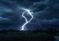 A dramatic photorealistic image of a powerful lightning strike during a nighttime thunderstorm, illuminating dark storm clouds with a bright branching electrical discharge connecting cloud to ground,
