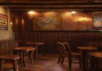 A cozy, dimly lit Spanish bar interior with wooden tables, vintage posters on the walls, and a small stage with musical instruments. A brass plaque on the wall reads 'Aquí nació Hombres G' in elegan