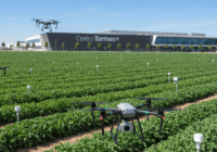 A photorealistic image of a high-tech agricultural field in Salamanca, Spain, with drones flying over green crops and sensors on the ground. The background shows a modern research center with the sign