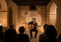 A musician, Carlos Ares, performing an intimate acoustic concert in a rustic stone-walled venue in Zamora, Spain, with warm candlelight and a small audience enraptured, surrounded by medieval architec