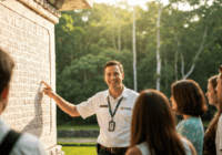 A professional tour guide standing in front of the Temple of the Inscriptions in Palenque, wearing a official badge, smiling, with a small group of tourists listening attentively, lush jungle backgrou