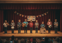 A group of children on a stage in a local community center, holding various musical instruments, smiling nervously while parents in the audience applaud. Warm lighting, photorealistic, candid moment.