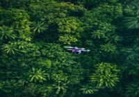 Aerial view of a drone flying over a dense tropical rainforest, equipped with a camera and sensors, monitoring wildlife from above, photorealistic, vibrant green colors, no text or logos.