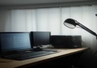 A modern home music studio with a laptop running Python code, a MIDI keyboard, studio monitors and a microphone on a boom arm. The screen shows waveform and code, soft ambient lighting, photorealistic